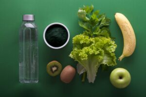 Healthy foods and water bottle on green background.