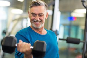 A mature man lifting a dumbbell at the gym with a smile.