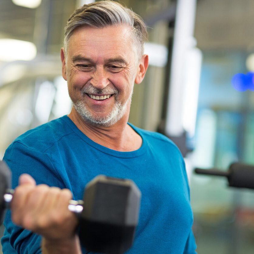 Senior man in health club A mature man lifting a dumbbell at the gym with a smile.