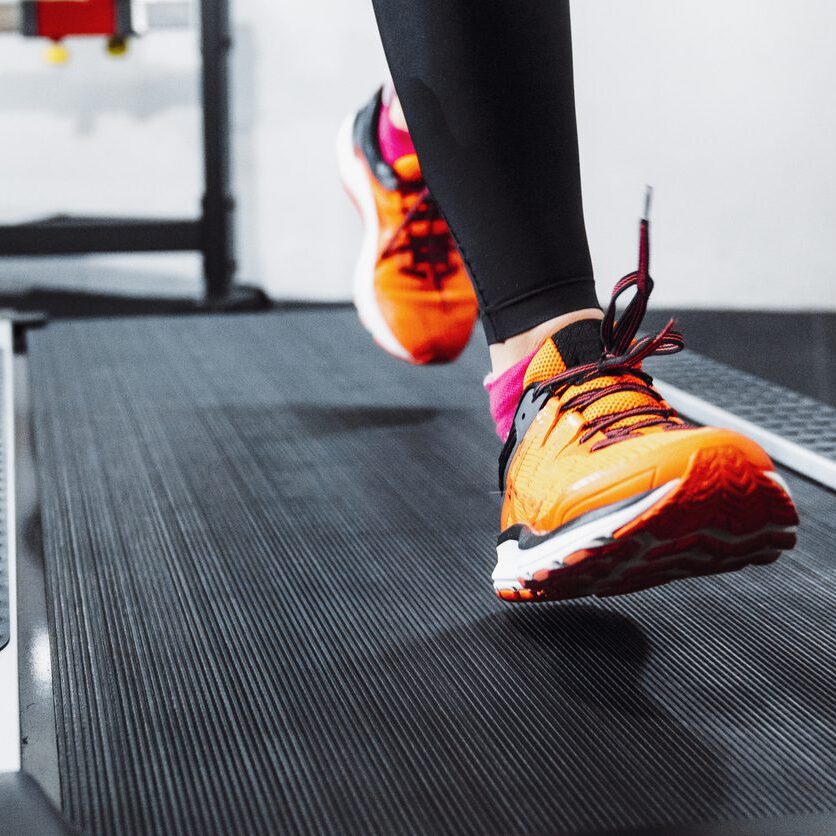 Close-up of orange running shoes on a treadmill.